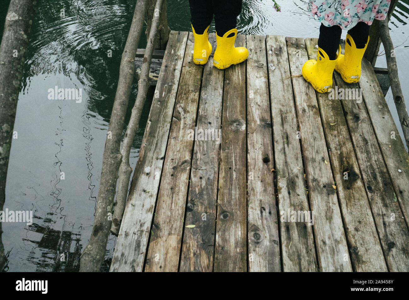 Zwei Kinder in regen Stiefel stehen auf einem Pier mit einem Teich. Stockfoto