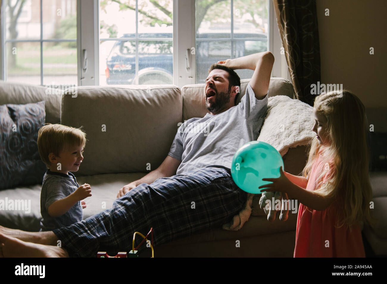 Eine müde Vater liegt auf der Couch, während seine Kinder um ihn herum spielen. Stockfoto