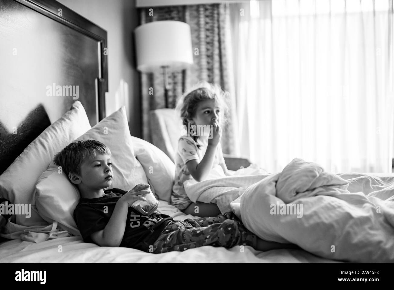 Zwei Kinder liegen in einem Hotel Zimmer Bett Snacks essen. Stockfoto