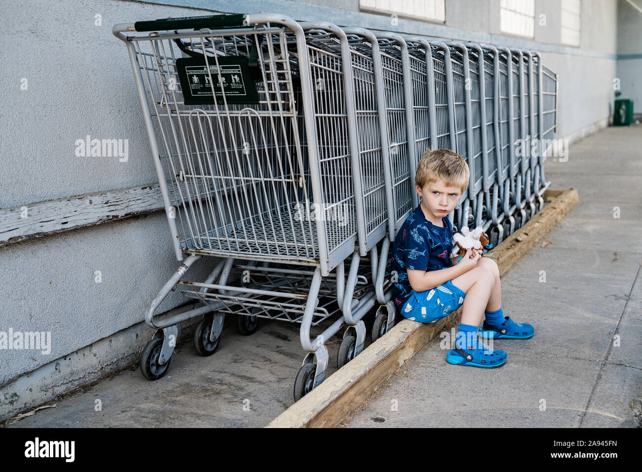 Ein kleiner Junge schmollt neben einer Reihe von Shopping Carts. Stockfoto