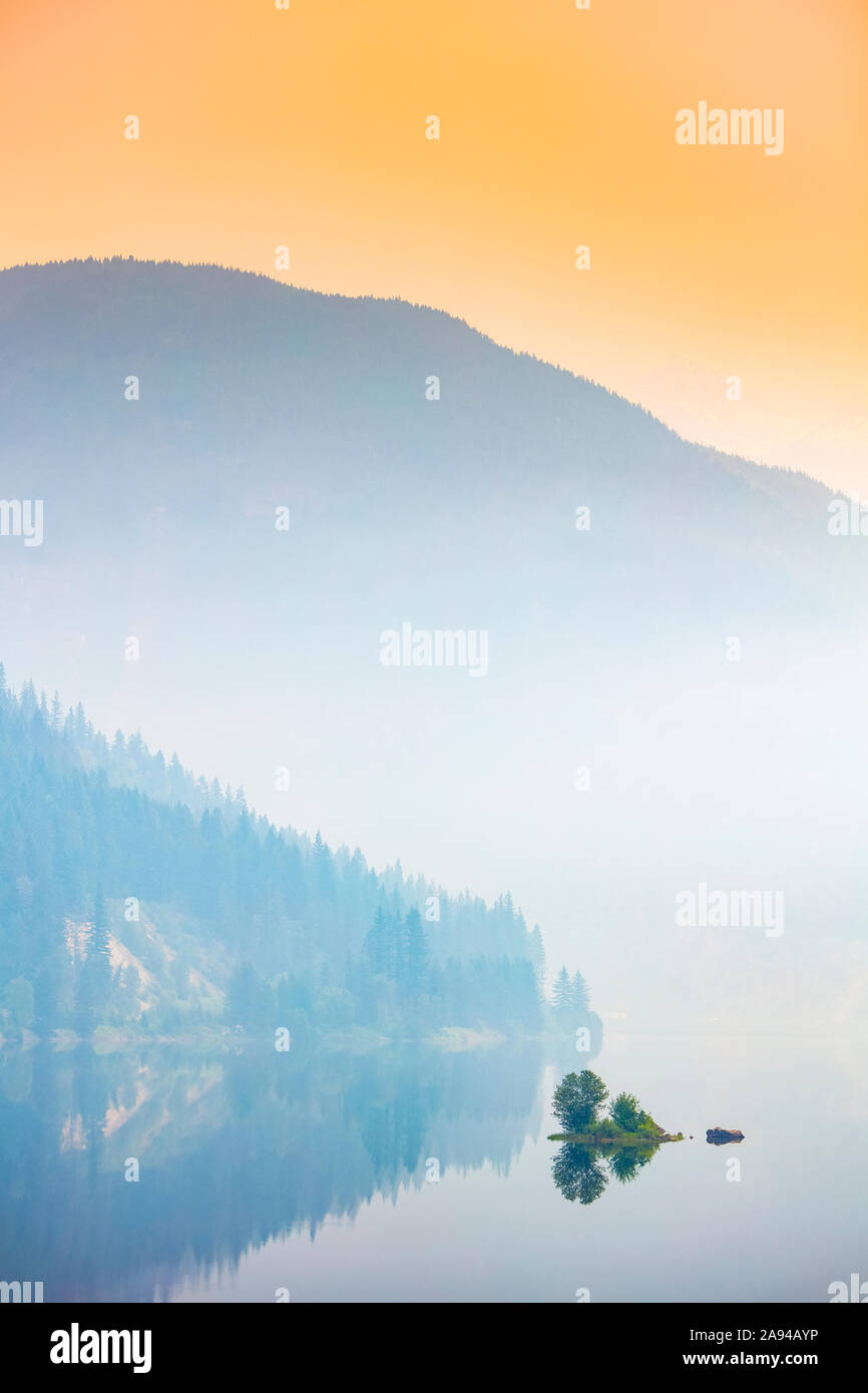 Dichter Nebel über einem See und einem Berg mit einem leuchtend orangefarbenen Himmel bei Sonnenaufgang; British Columbia, Kanada Stockfoto