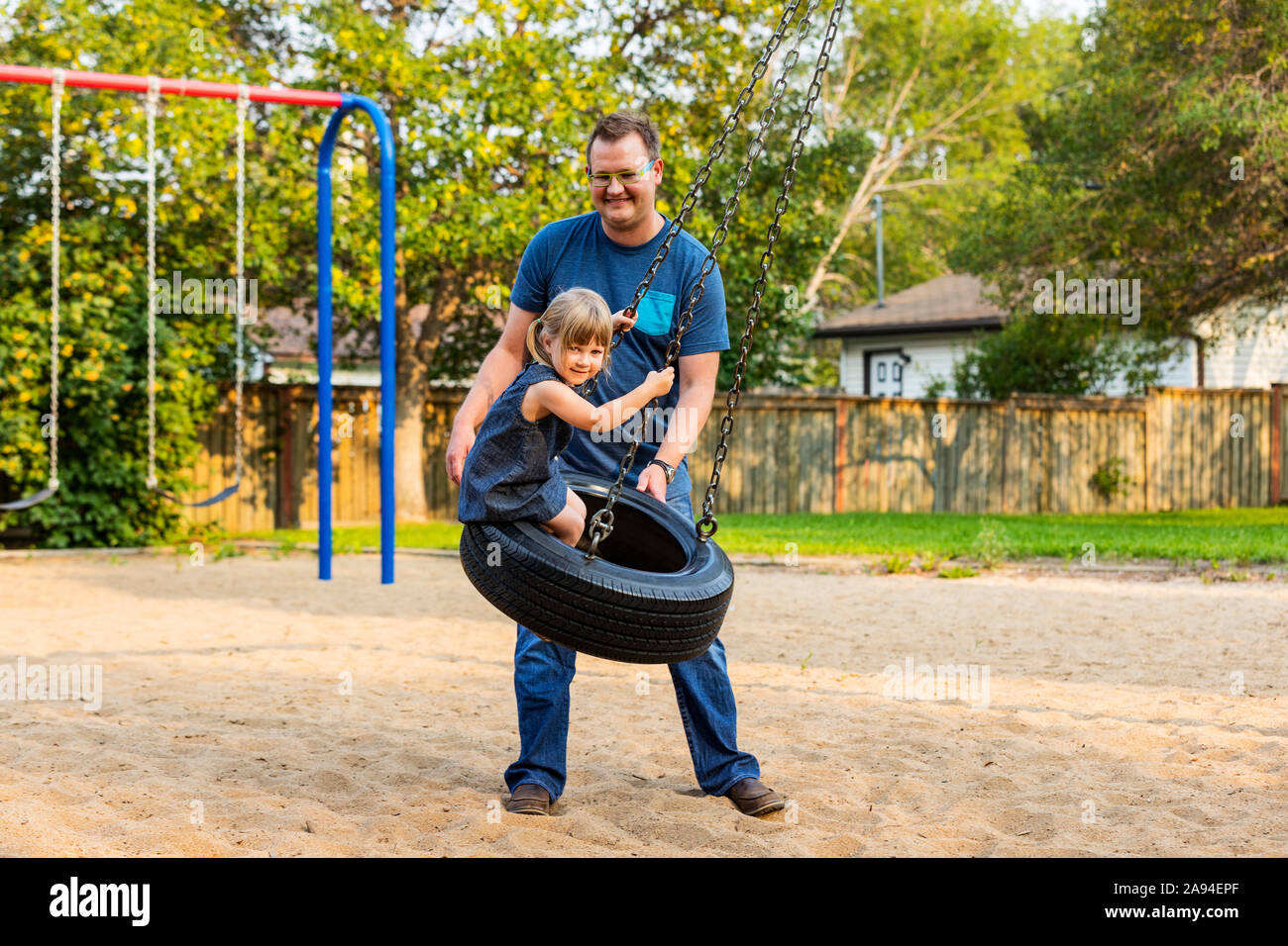 Ein Vater schiebt seine Tochter auf einer Reifenschaukel auf einem Spielplatz; Edmonton, Alberta, Kanada Stockfoto