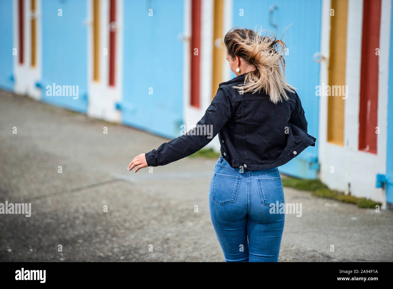 Eine junge Frau geht die Straße hinunter mit windgeblasenem Haar und formschlüssigen Jeans; Wellington, Nordinsel, Neuseeland Stockfoto