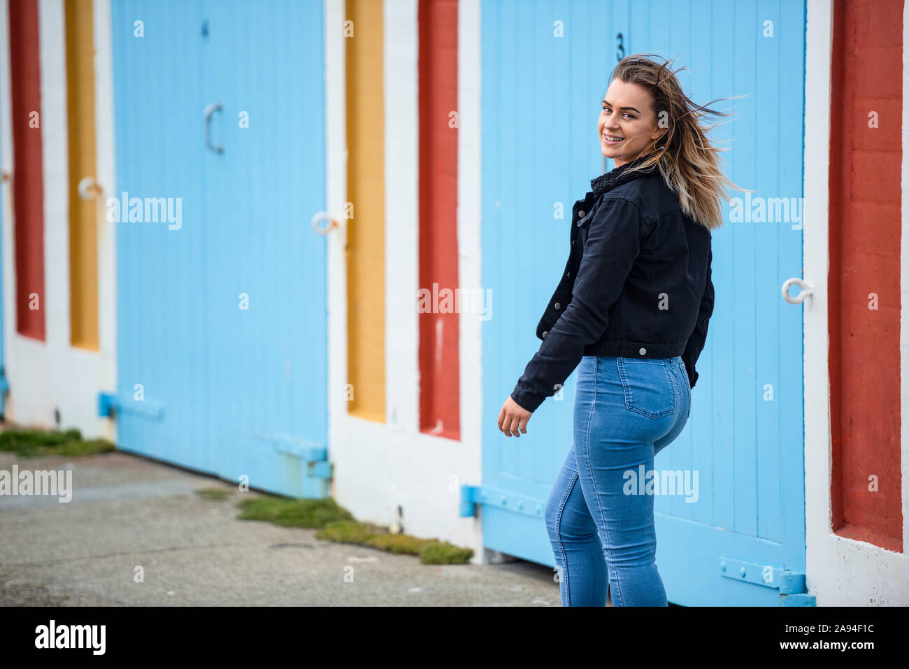 Eine junge Frau geht die Straße entlang eines bunten Gebäudes und blickt über ihre Schulter auf die Kamera; Wellington, Nordinsel, Neuseeland Stockfoto