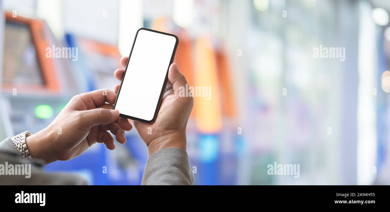7/8 Schuß des Young Professional Geschäftsmann holding Blank Screen Smartphone mit unscharfen Geldautomaten Hintergrund Stockfoto