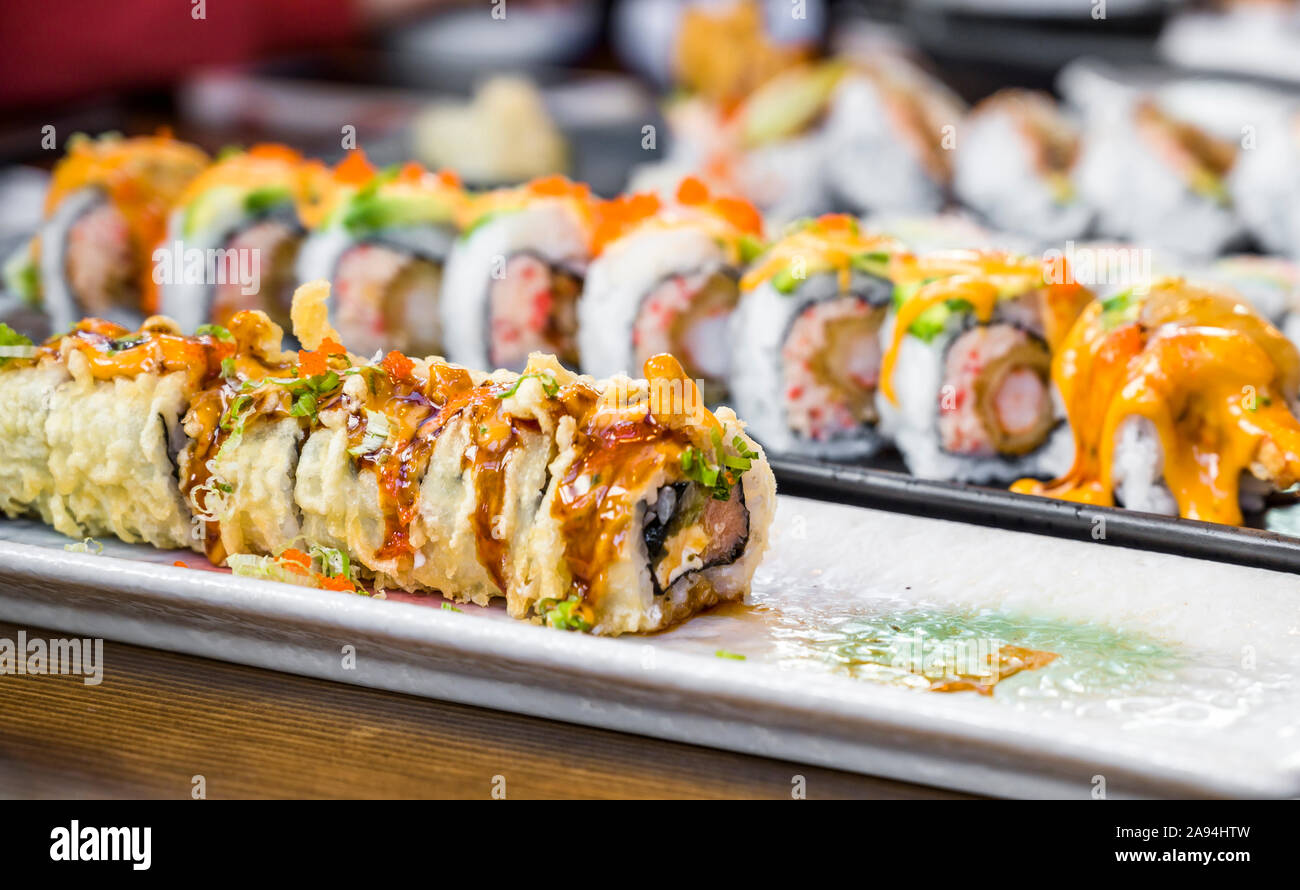 Platten mit verschiedenen Arten von fachmännisch zubereitet und in Scheiben geschnittenen Sushi mit Gewürzen und Saucen sind auf Esstisch köstlich und diätetische zu genießen angezeigt Stockfoto