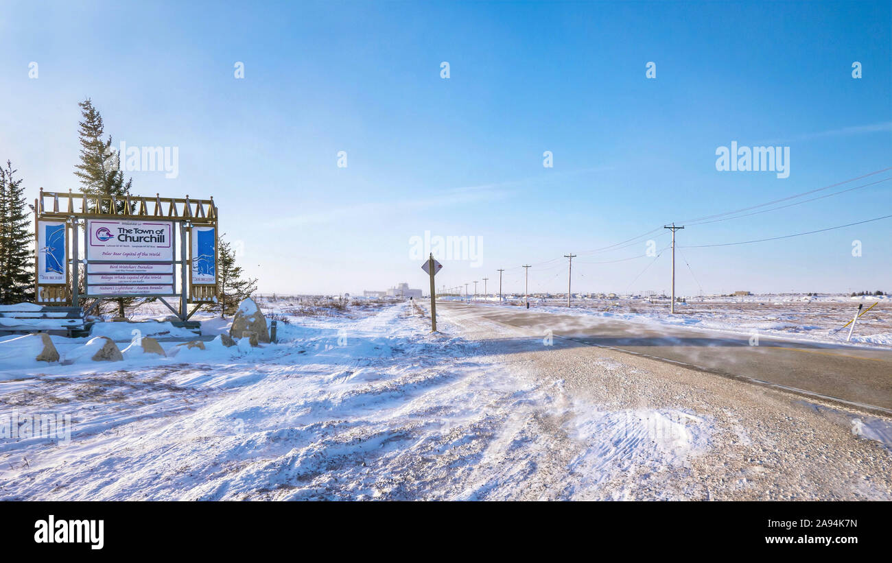 Schnee wird über eine Landstraße neben einem Touristen willkommen Schild in der Nähe der nördlichen Stadt Churchill, Manitoba, Kanada. Stockfoto