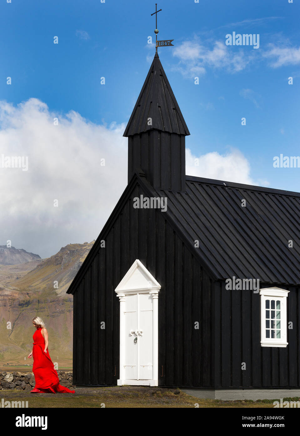 Isländische Blondine im roten Kleid bei Budir Kirche aus schwarzem Holz Struktur von 1847 auf der Halbinsel von Island sitzen Snaefellsnese Stockfoto