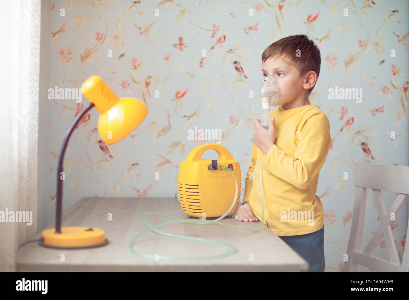 Health Care Konzept der kranken Kleinen kaukasischen Junge im gelben Hemd holding Inhalator in der Nähe von seinem Gesicht Atmung Dampf für die Behandlung zu Hause. Stockfoto