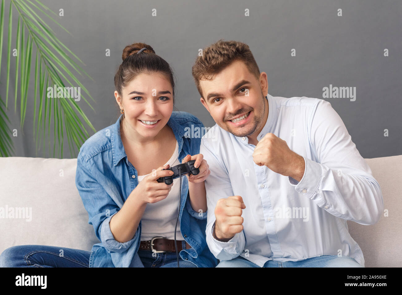 Relationnship Konzept. Junges Paar Mann die Frau spielen video game Lächeln locker sitzen auf einem Sofa studio isoliert auf Grau Stockfoto