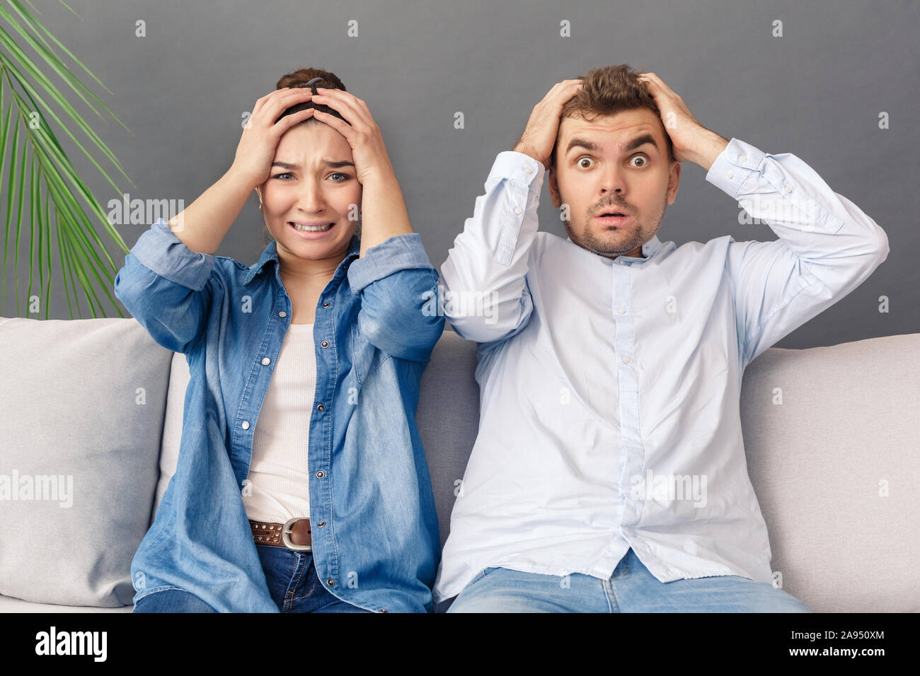 Relationnship Konzept. Junges Paar sitzt auf einem Sofa Studio auf Grau holding Kopf isoliert schockiert Stockfoto