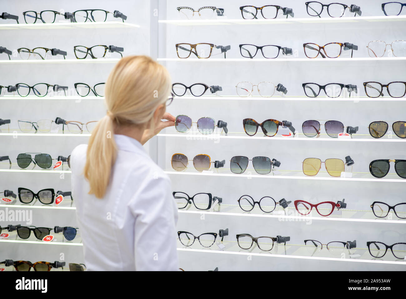 Gläser auf Regalen. Blonde Augenarzt tragen weiße Fell Gläser setzen auf Regalen in optischen Speichern Stockfoto