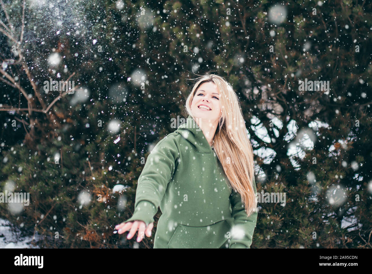 Schöne junge Frau wirft Schneeball - Outdoor Portrait im Winter bei Schneefall - attraktive Blondine Spaß hat Stockfoto