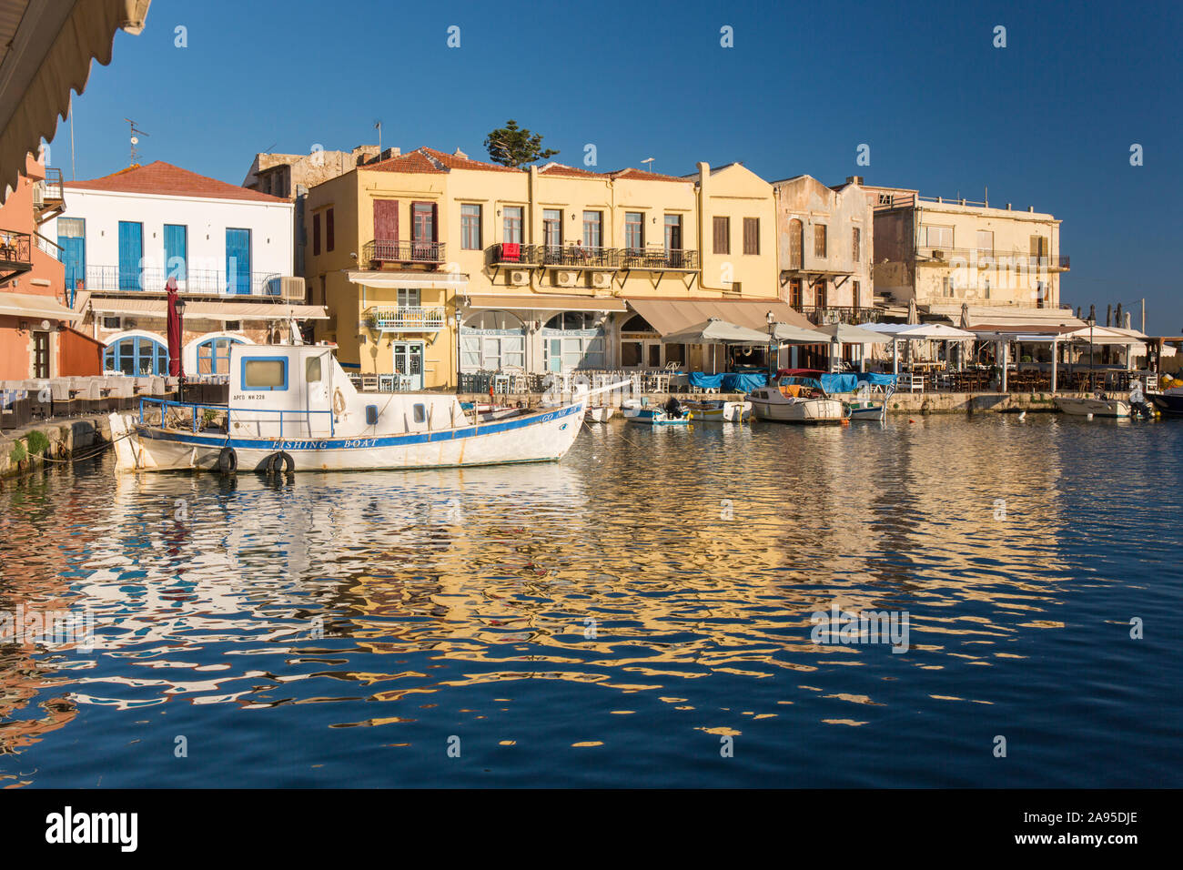 Rethymno, Kreta, Griechenland. Blick über den venezianischen Hafen, am frühen Morgen, Gebäude am Wasser reflektiert in gewelltem Wasser. Stockfoto