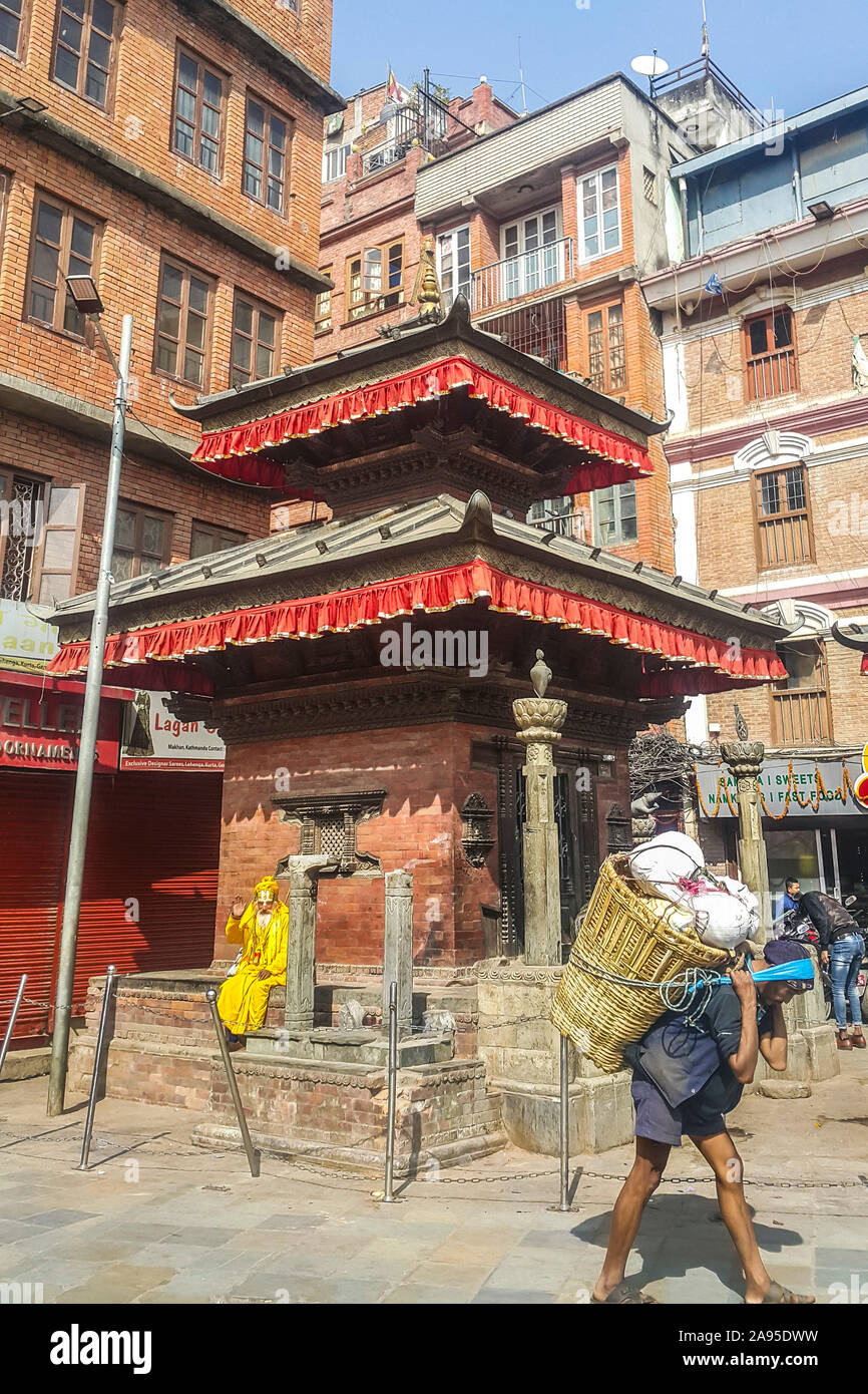 Lokale Szene in der Nähe des Durbar Square, Kathmandu, Nepal mit einem Hindu Swami Entspannung von einem Hindu Schrein und winkende Passanten Stockfoto
