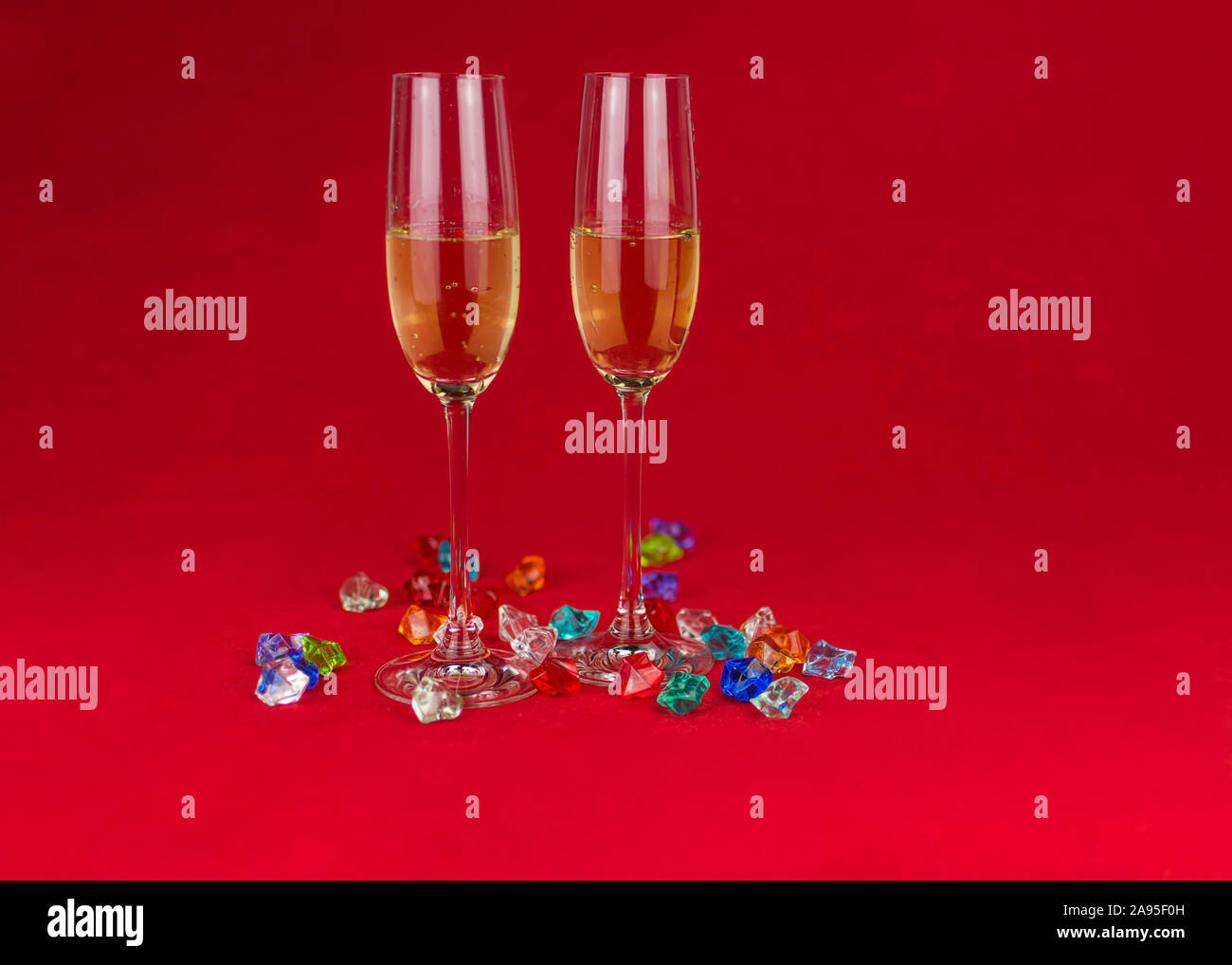 Gläser Champagner auf rotem Hintergrund und funkelnden Schmucksteinen auf Basis von Ant im Vordergrund. Neues Jahr oder romantische Feier. Luxus. Freier Speicherplatz Stockfoto