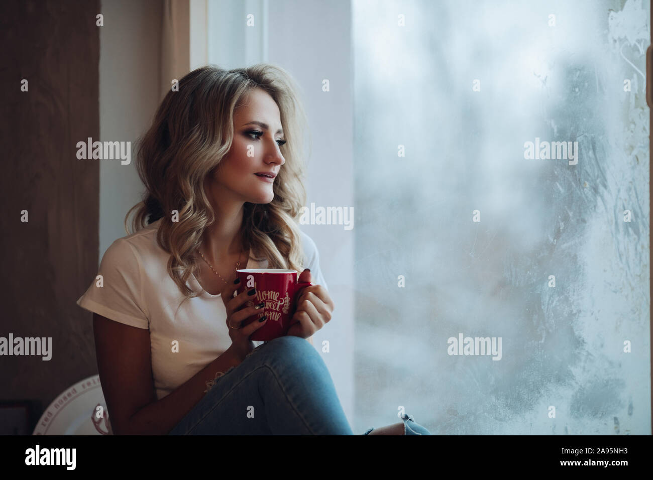 Schöne Blondine sitzen auf Fensterbank mit Becher. Stockfoto