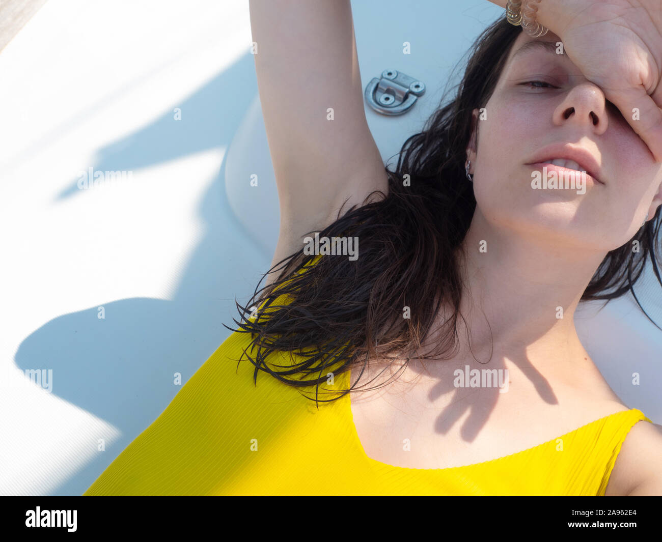 Junge Frau in einem hellen Gelb einteiligen Badeanzug Sonnenbaden an Deck einer Segelyacht. Urlaub am Meer, Sonnenbrand und Sonnenschutz. Stockfoto