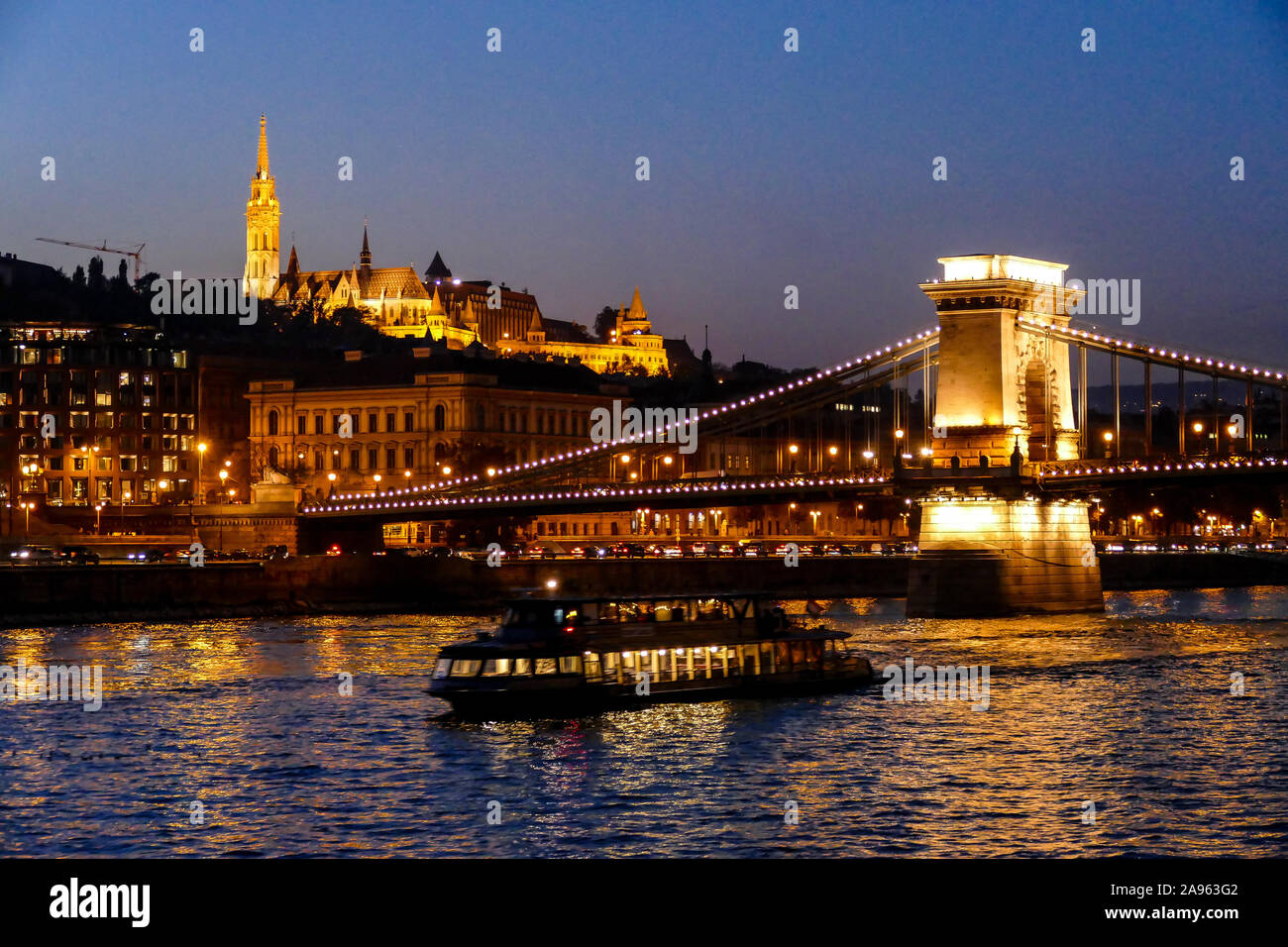 Die Chain Bridge bei Nacht beleuchtet mit Schloss Buda und die Turmspitze der Matthias Kirche im Hintergrund Stockfoto