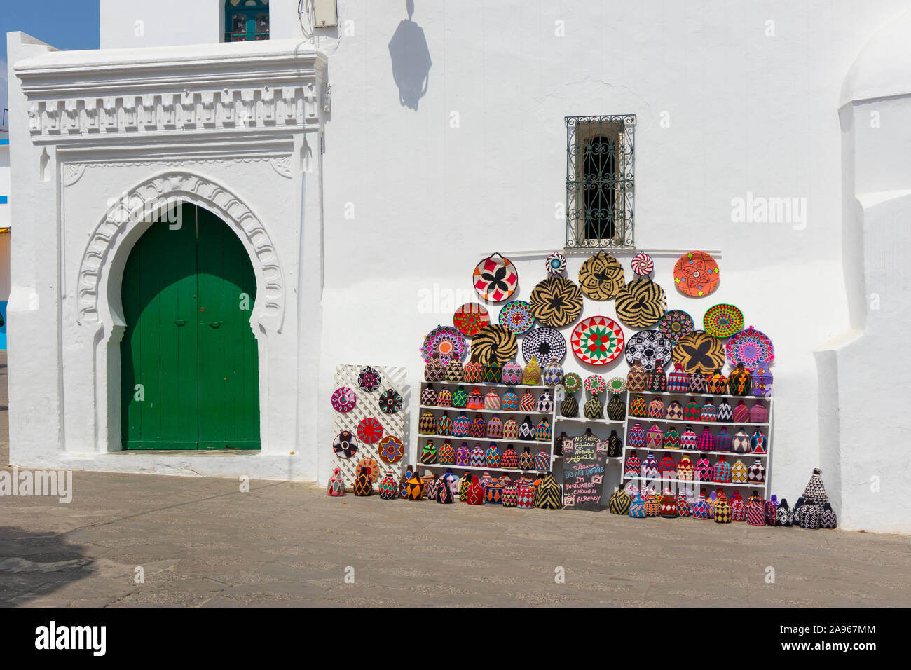 Asilah, Morocco-September 10, 2019: bunt verziert Souvenirs an der Wand neben einem traditionellen Tür in der Medina von Ouarzazate, Marokko zeigte Stockfoto