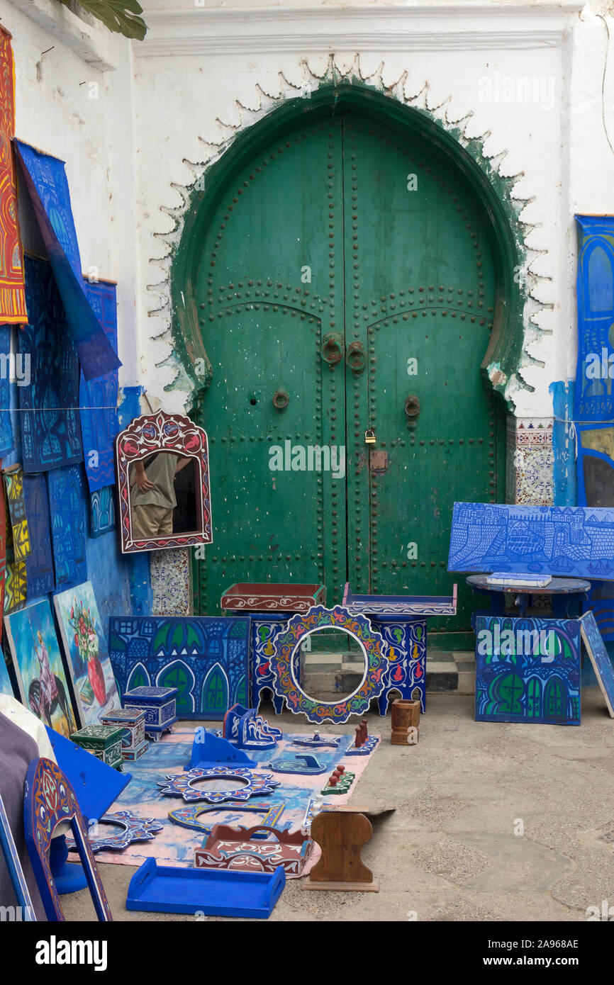 Asilah, Morocco-September 10, 2019: Verkauf von hausgemachten Kunst vor einer traditionellen historischen Tür in der Medina, der Altstadt von Asilah Stockfoto