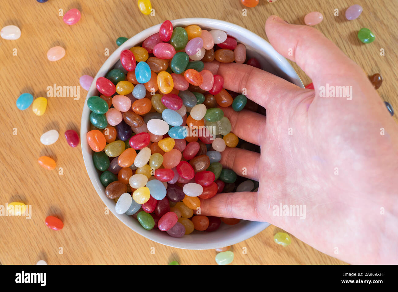 Die Hände eines erwachsenen Mannes scooping Jelly Beans in eine Schüssel voller Geleebonbons. Konzept, sucht nach Süßigkeiten, Süßwaren, Süßigkeiten, Freuden des Lebens Stockfoto