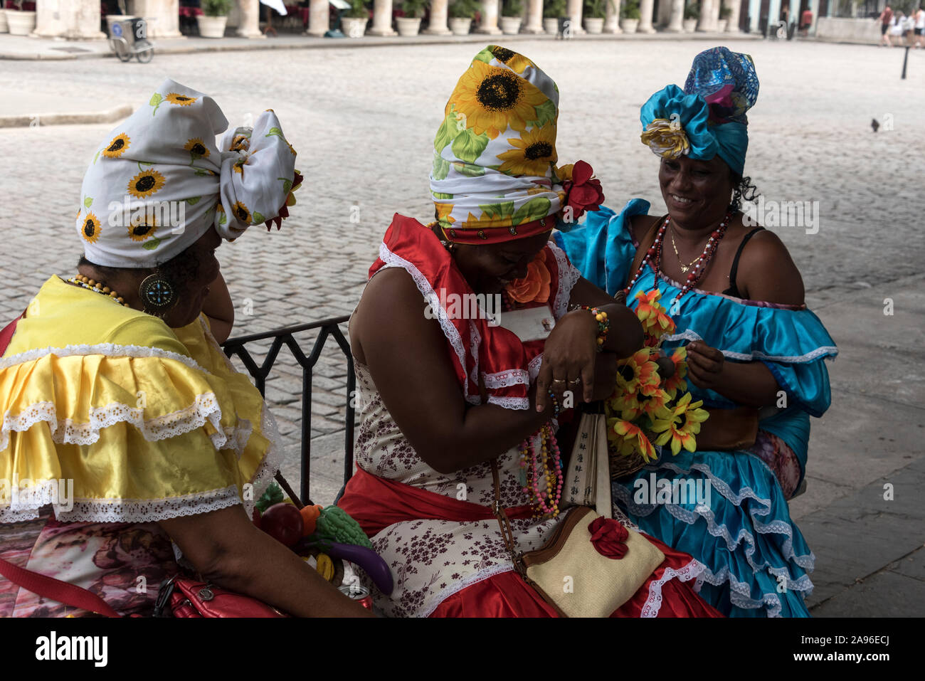 Drei kubanische Frauen in farbenfrohen Kolonialkleidern, bereit, für Touristenfotos für ein paar Münzen zu posieren. Sie nehmen eine kurze br Stockfoto