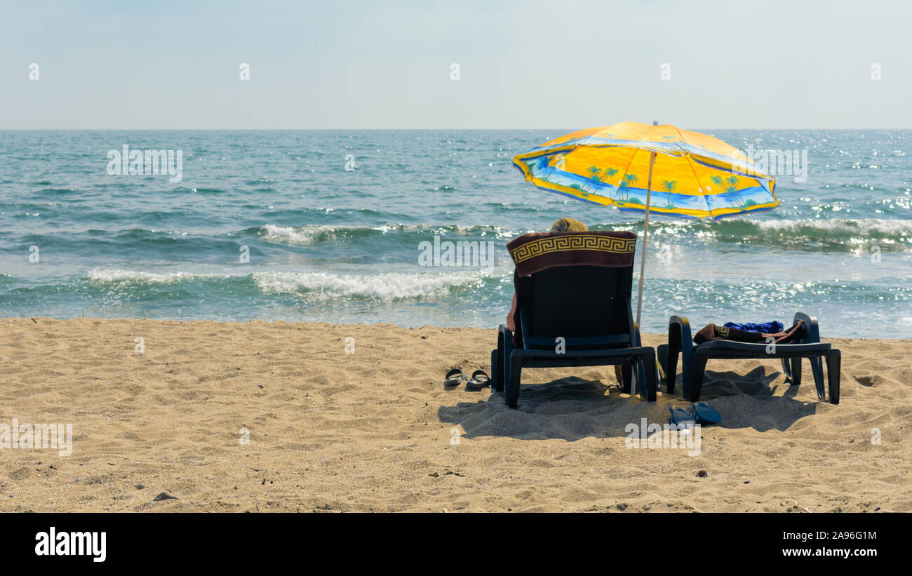 Die Menschen auf den Sonnenliegen unter einem Sonnenschirm am Strand gegen das Meer entspannen Stockfoto