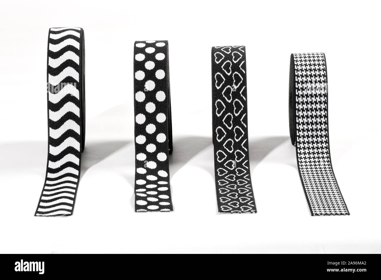 Vier verschiedene schwarze und weiße Dekorative elastische Bänder oder Streifen in Rollen in einer Linie über einen weißen Hintergrund mit Fischgrätmuster, Streifen angezeigt, hea Stockfoto