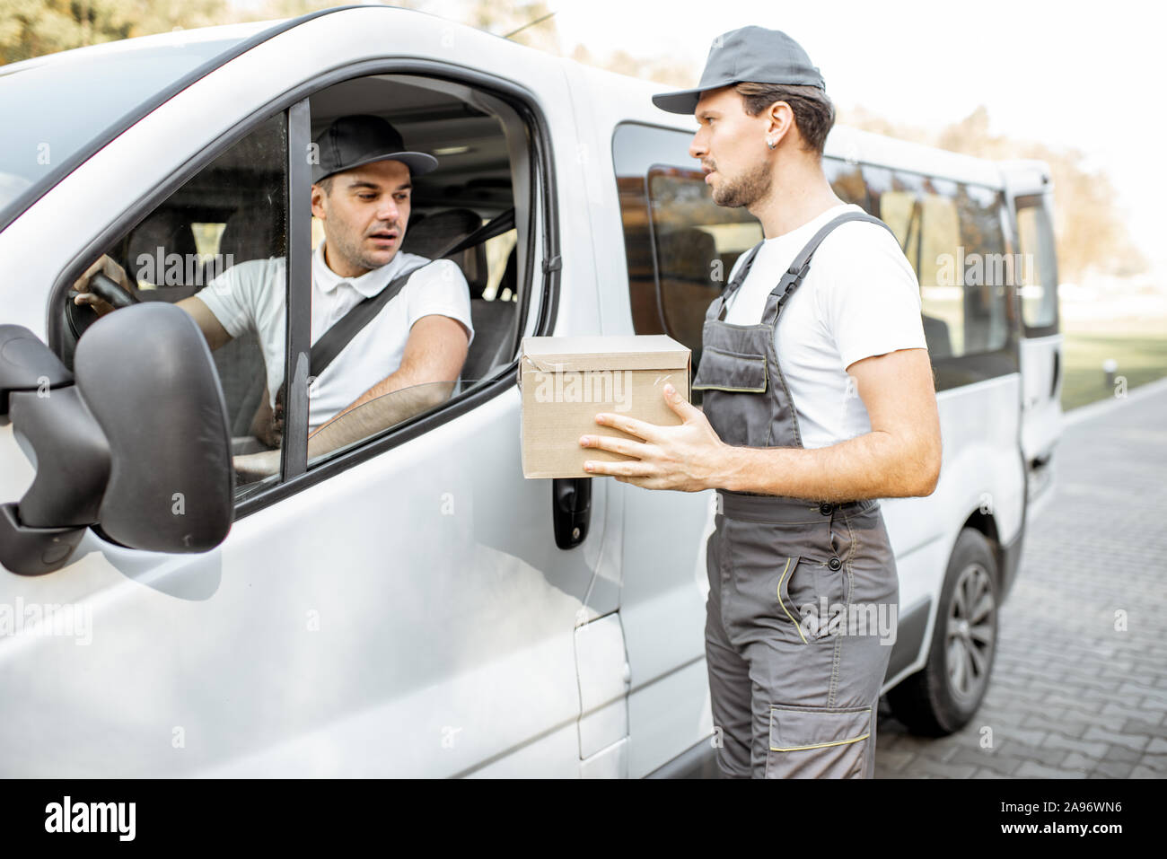 Lieferung Unternehmen Mitarbeiter in Uniform Lieferung von Cargo van Fahrzeug, Mover mit Paket im Gespräch mit einem PKW-Fahrer Stockfoto