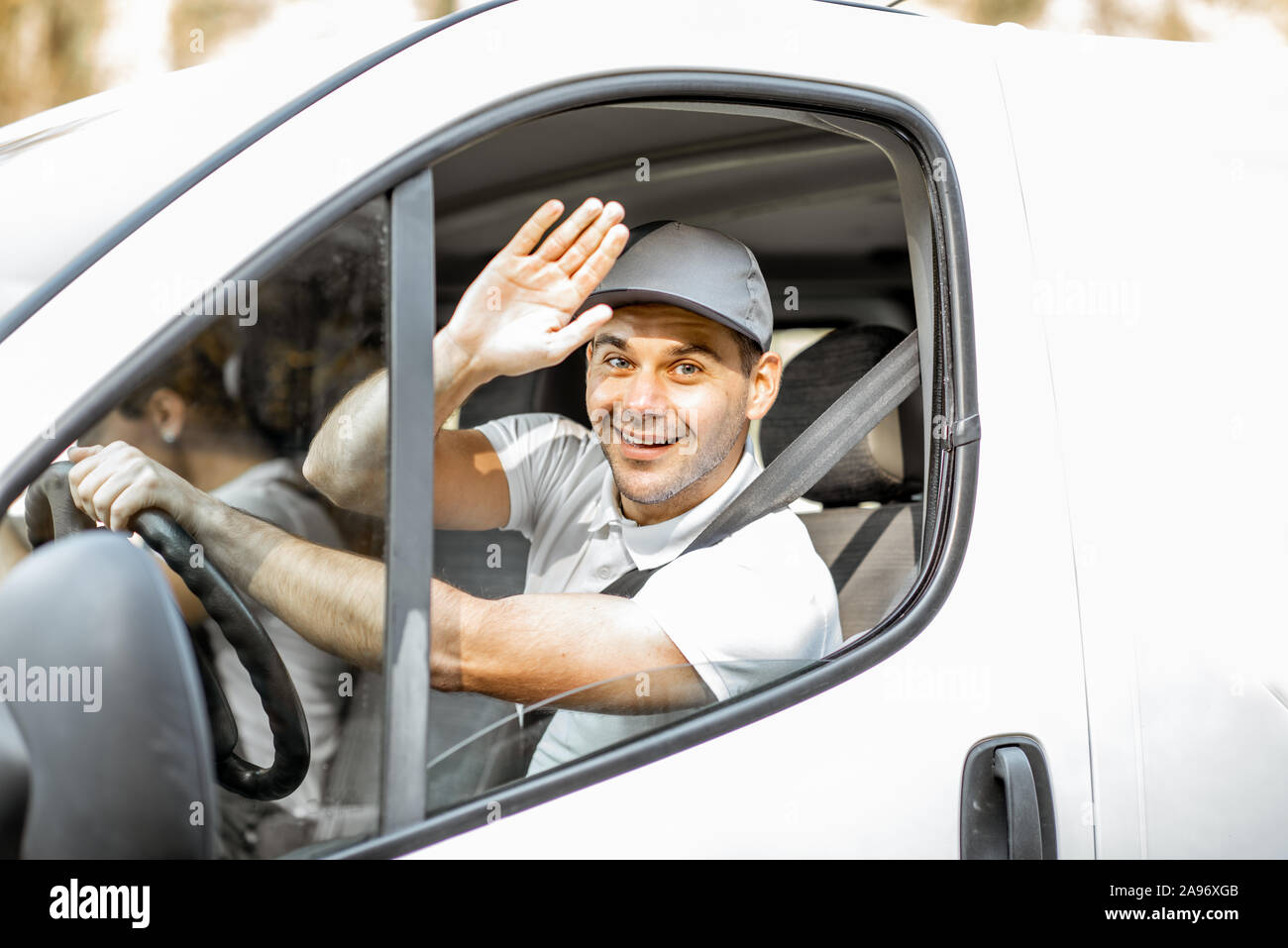 Porträt einer fröhlichen Anlieferung Treiber in Uniform Blick aus dem Fenster des weißen Lieferwagen vahicle, Lieferung mit dem Auto Stockfoto