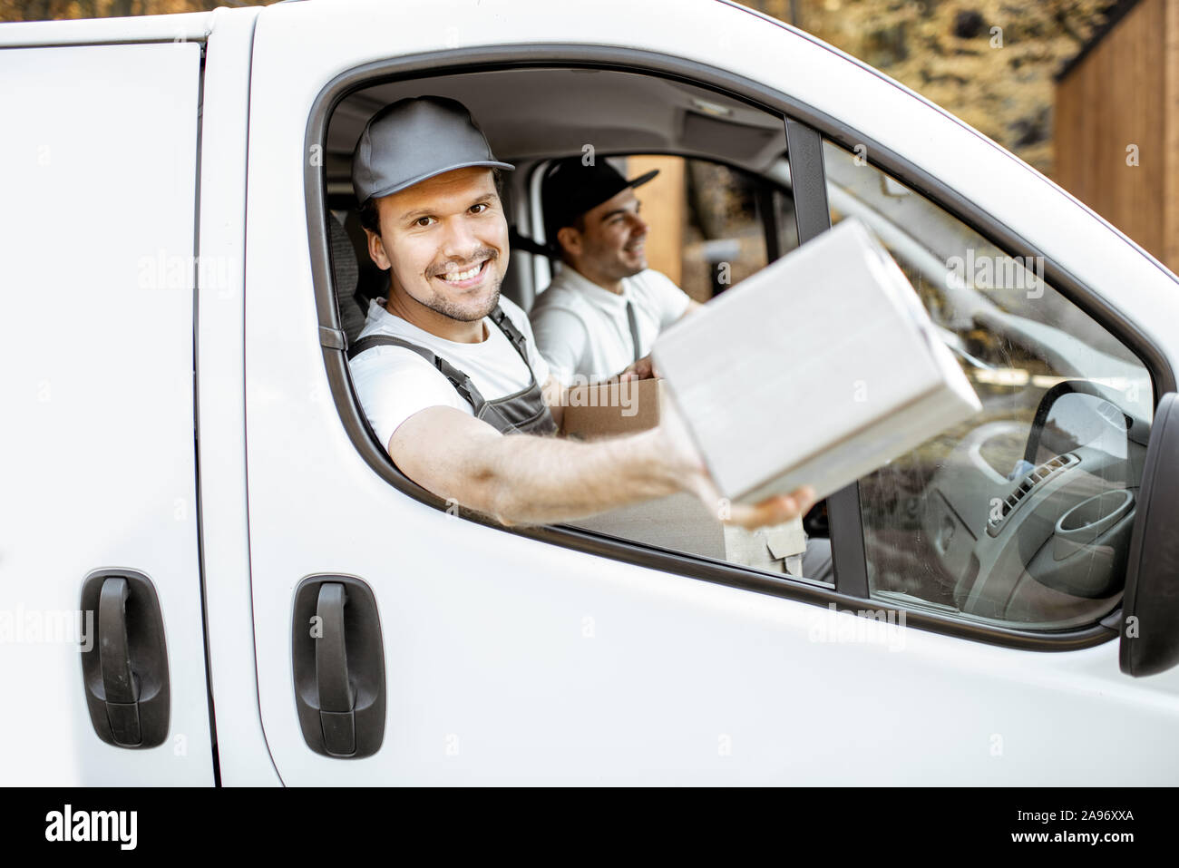 Freundliche Lieferung Mitarbeiter in Unternehmen, die Ware an den Kunden auf einer Ladung Fahrzeug, stattlich Kurier Blick aus dem Fenster mit einem Paket Stockfoto