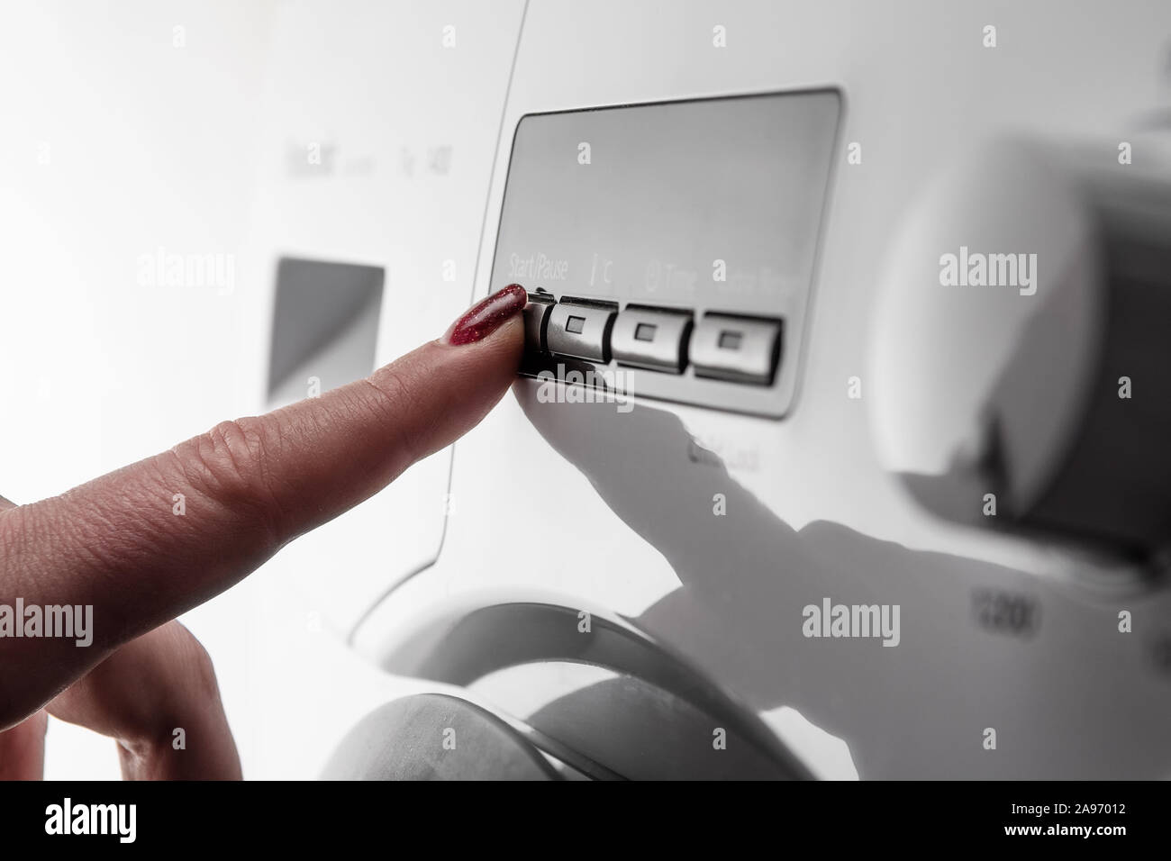 Closeup Detail der Frau Zeigefinger mit Nagellack drücken Taste auf weißes modernes Waschmaschine starten Stockfoto