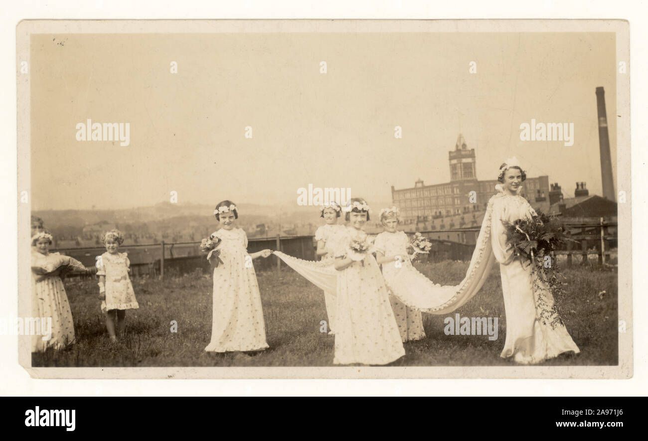 Originalfoto des Karnevals der Rosenkönigin aus dem frühen 20. Jahrhundert von der St. Thomas School, Halliwell, Bolton - hier mit der frisch gekrönten Rosenkönigin und ihren Begleitern, die den Zug ihres Kleides halten, an einem traditionellen „Walking Day“. Die Baumwollfabrik von Falcon befindet sich im Hintergrund, Greater Manchester, Großbritannien, um 1940 Stockfoto