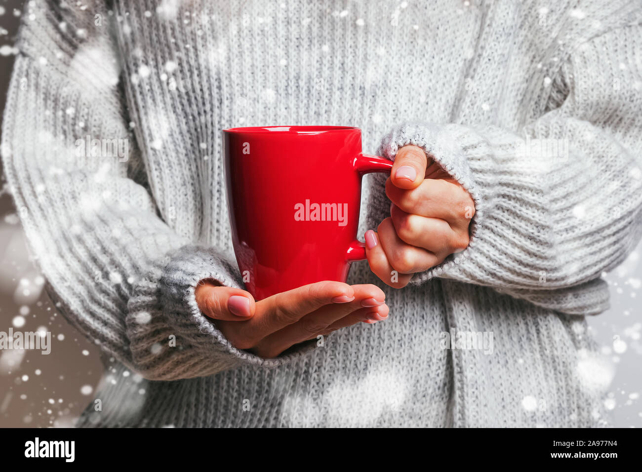 Weibliche Hände in Form gestrickter Pullover mit roten Becher mit heißem Tee, Kaffee oder Kakao. Stockfoto