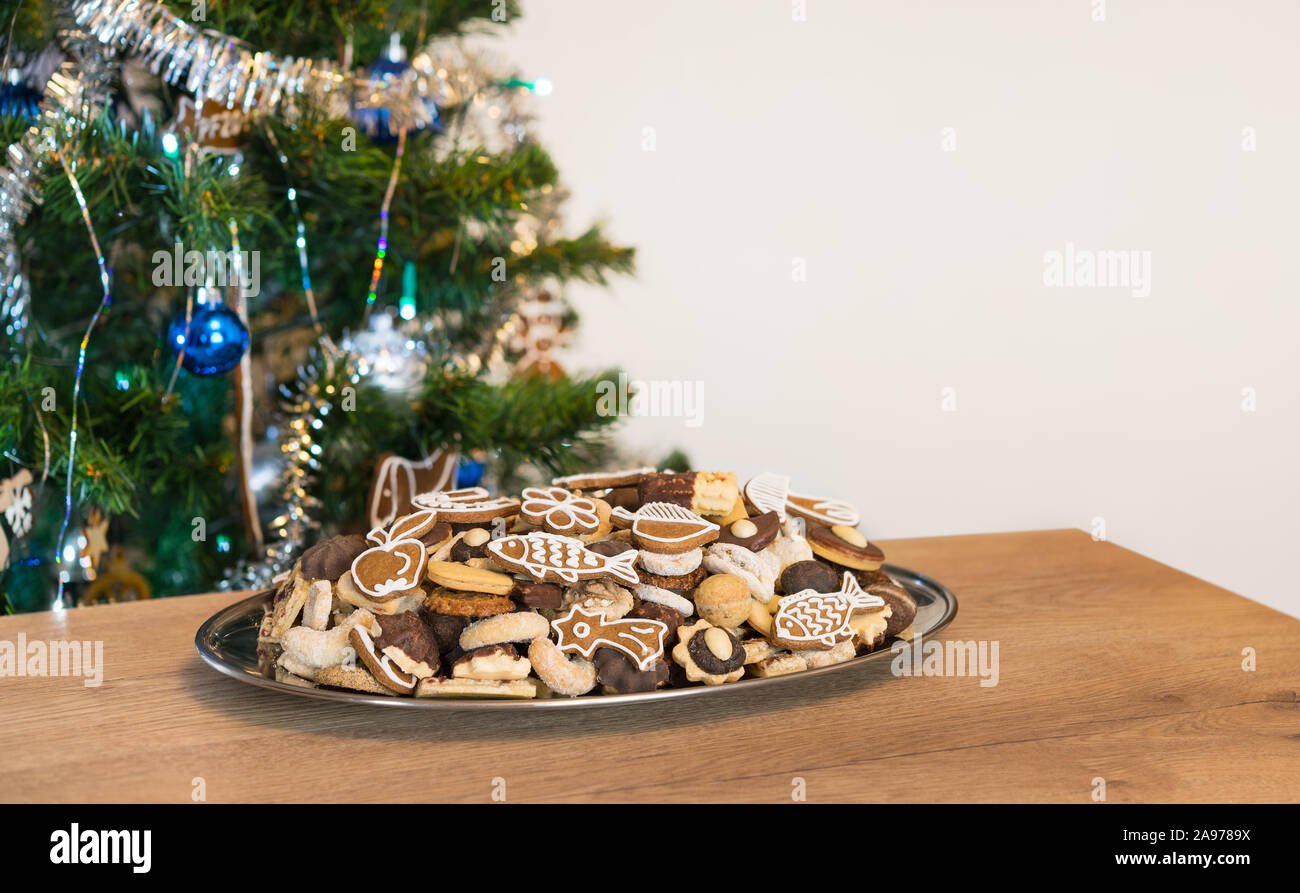 Dekoriert grün Weihnachtsbaum. Verschiedene Cookies in silbernen Tablett auf Holz Tisch. Stillleben mit Weihnachten und Neujahr in Stimmung. Kopieren Sie Speicherplatz auf weißen Hintergrund. Stockfoto