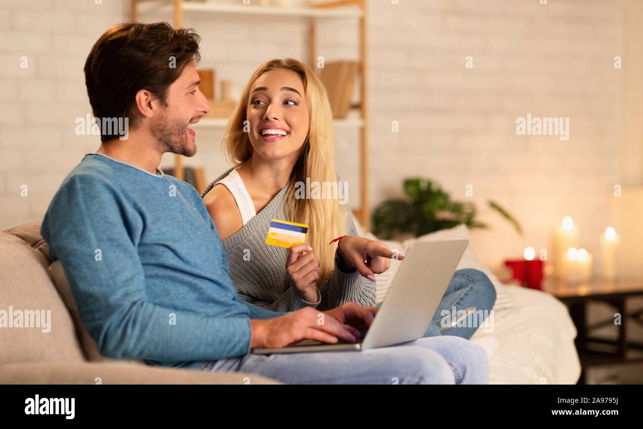 Glückliches Paar Online Einkaufen, die auf Notebook- und Zahlung mit Kreditkarte Einkaufen im Internet Sitzen auf einem Sofa zu Hause Stockfoto
