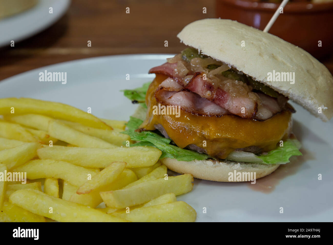 Isolierte Bild von Kalbfleisch Burger mit Pommes frites auf weiße Platte auf hölzernen Hintergrund serviert. Stockfoto