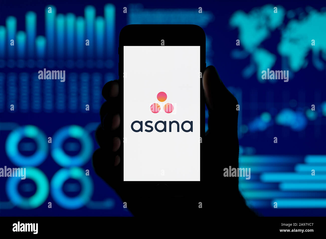 Ein Mann hält ein iPhone, das zeigt die Asana logo, Schuß gegen eine Visualisierung von Daten im Hintergrund (nur redaktionelle Nutzung). Stockfoto