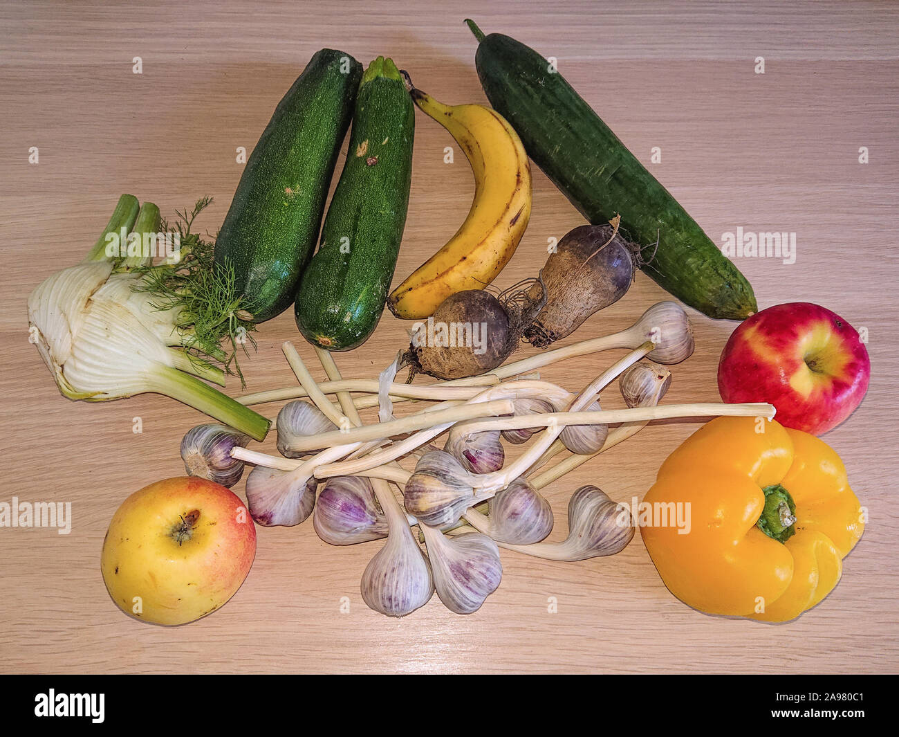 Verschiedene organische Gemüse und Früchte auf einem Holztisch - apple, Knoblauch, Banane, Paprika, Rote Bete, Fenchel, Zucchini und eine Gurke angeordnet Stockfoto
