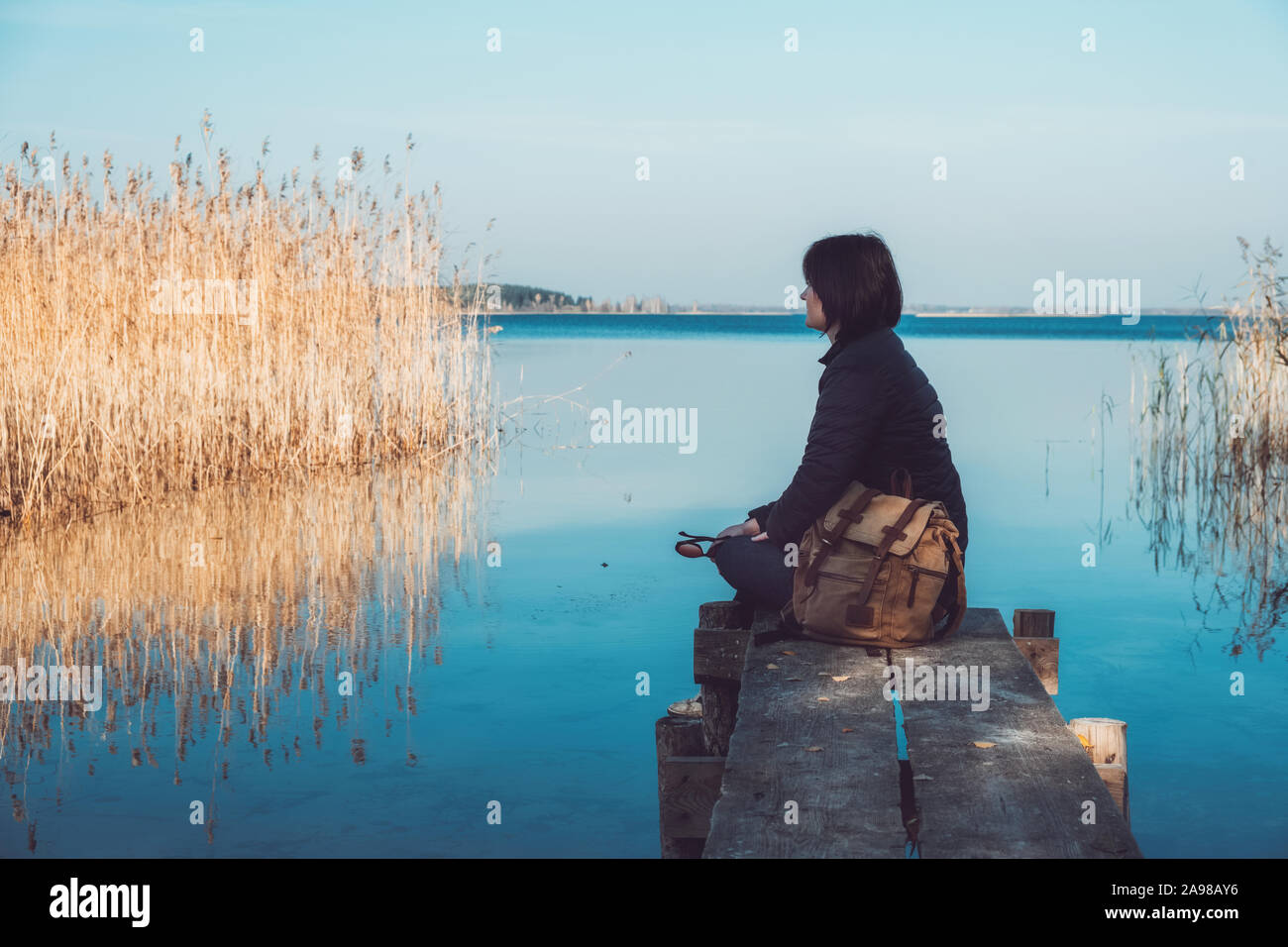 Touristische Frau mit Rucksack auf Holzbrücken auf ruhigen See. Stockfoto