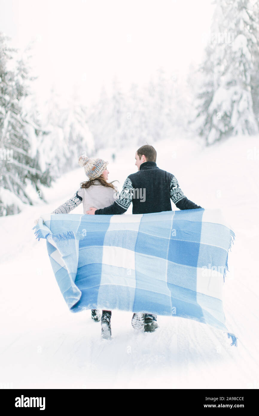 Junges Paar in der Liebe einen Spaziergang im Winter verschneite Wald und halten warme Wolldecke in Händen Stockfoto