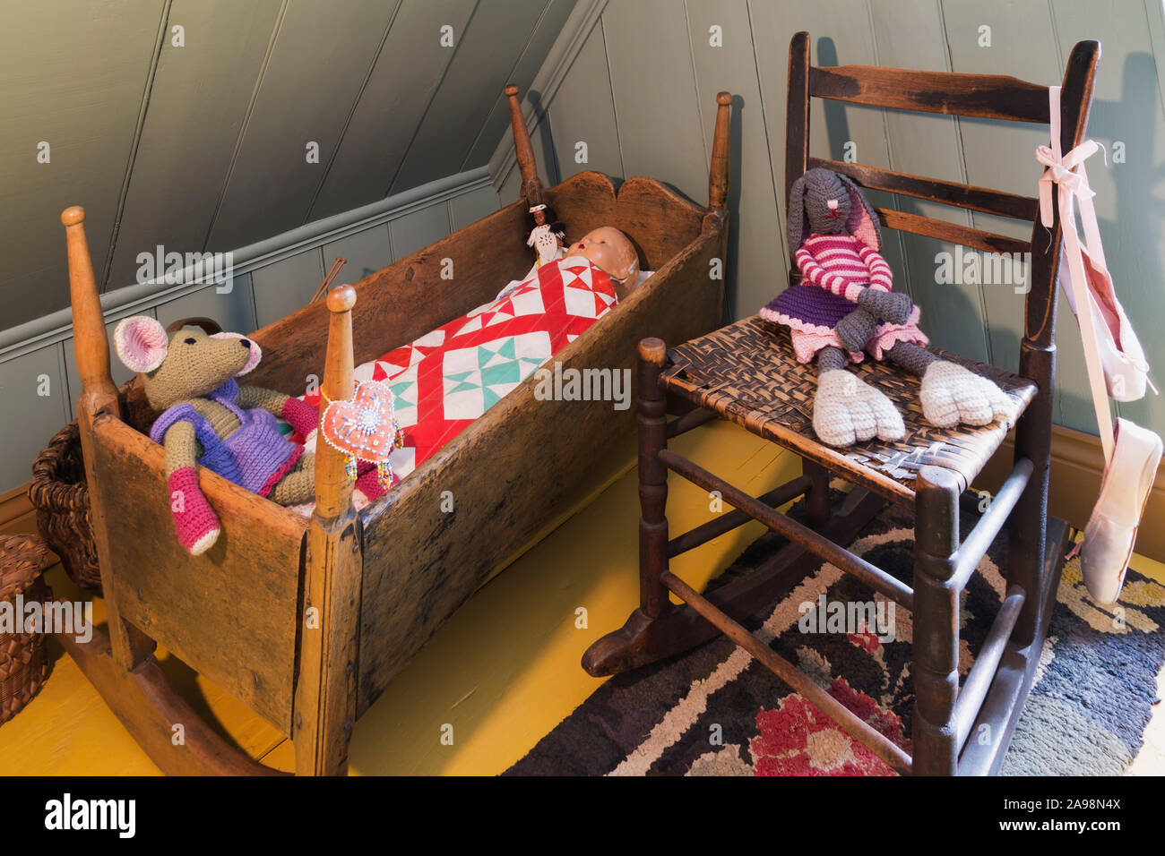 Antike hölzerne Krippe, gewebt Sitz Schaukelstuhl mit dem Kind Puppen im Master Schlafzimmer mit Gelb lackiert breite Diele Dielen in einem alten Haus Stockfoto