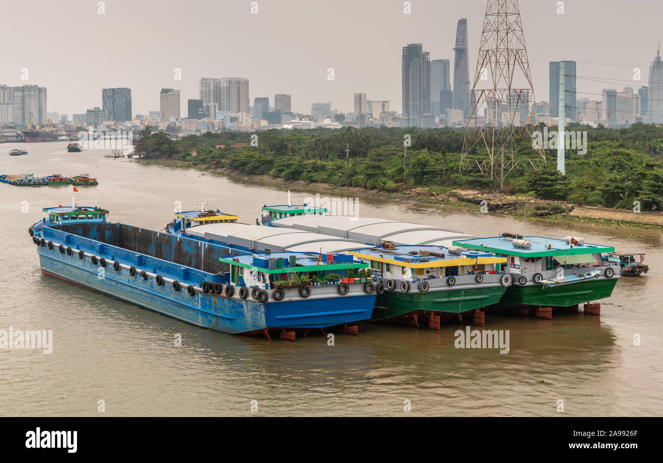 Ho Chi Minh City, Vietnam - 12. März 2019: Song Sai Gon River. Drei moderne große Lastkähne in braunem Wasser verankert. Silber Himmel, grünen Riemen und der Innenstadt Stockfoto