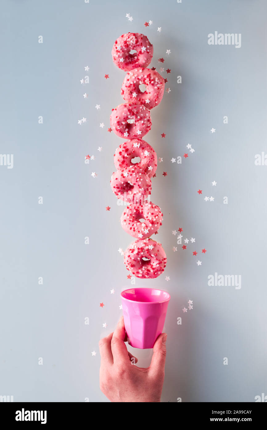 Kreative Bild der vollkommenen Balance, Turm oder der Pyramide von leckeren Rosa donuts Balancing über rosa Schale aus Kunststoff in weiblicher Hand. Beliebte hanuka Dessert. Konz Stockfoto