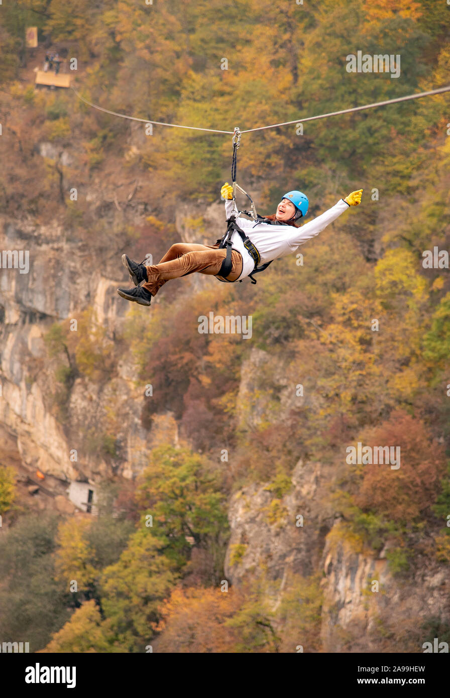 Eine Frau in einem Helm fliegt auf einer Seilrutsche über einen bunten Herbst Schlucht. Stockfoto