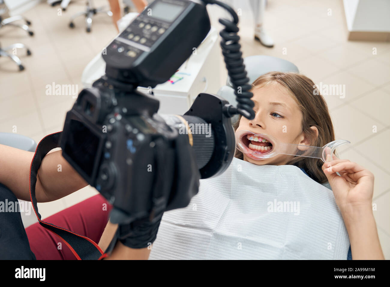 Mädchen besuchen Zahnklinik. Arzt Prüfung der Zähne des Patienten mit Sonderausstattung. Bold Patient im Behandlungsstuhl sitzen mit öffnen den Mund und halten den Mund Gurtaufroller. Stockfoto