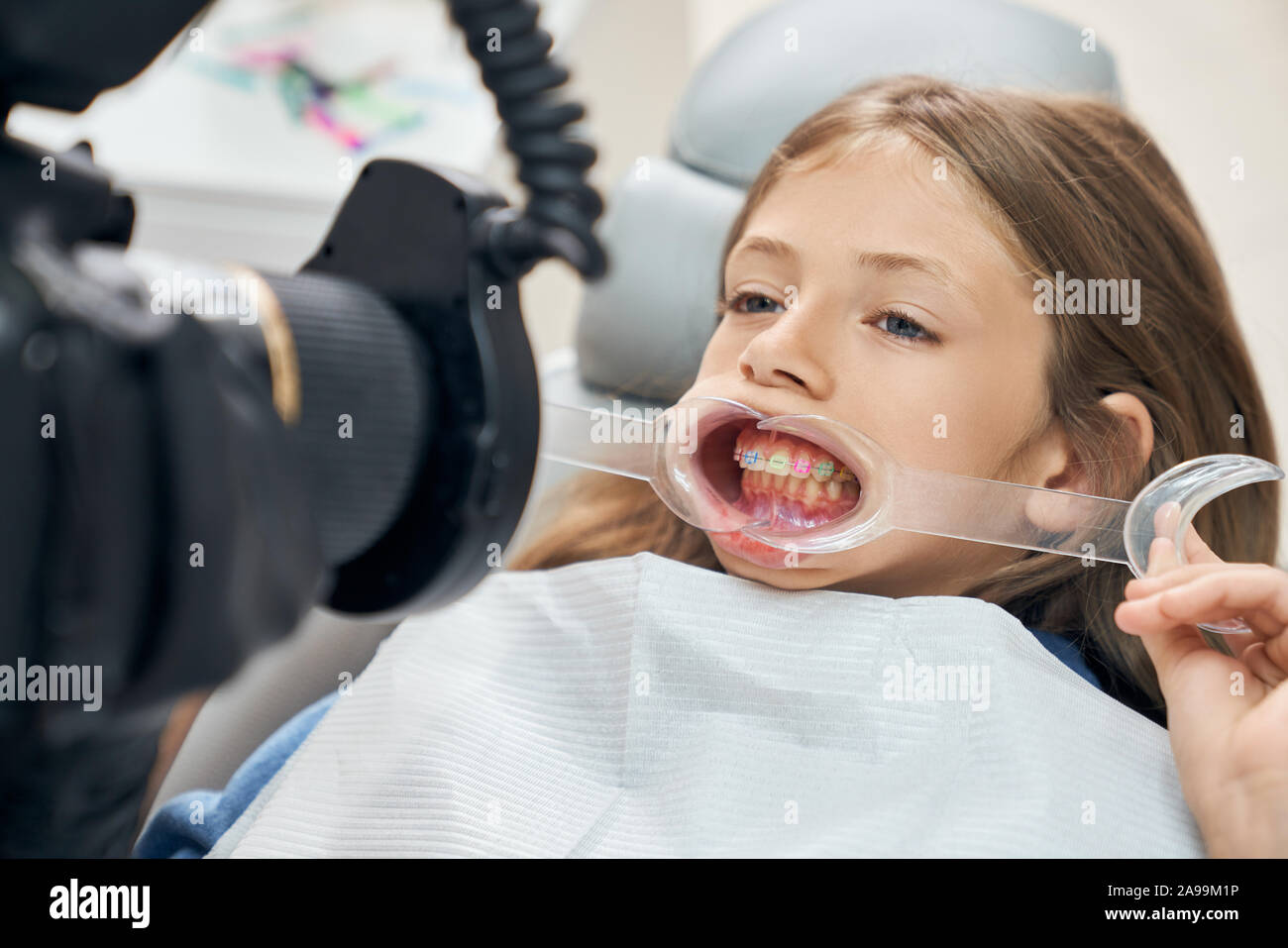 Nahaufnahme von bold Mädchen öffnen den Mund und halten den Mund Gurtaufroller. Junge Patienten in zahnmedizinischen Stuhl saßen und von der Kamera. Konzept des modernen "Untersuchung und Behandlung von Zähnen. Stockfoto
