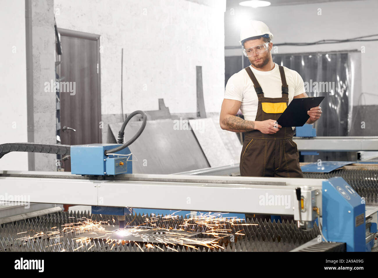 Ansicht von der Seite der ernster Mann in Schutzbrille und Helm, Ordner und Daten für die Steuerung von Geräten und Anlagen. Konzept der Plasma- und Metallarbeiten. Stockfoto