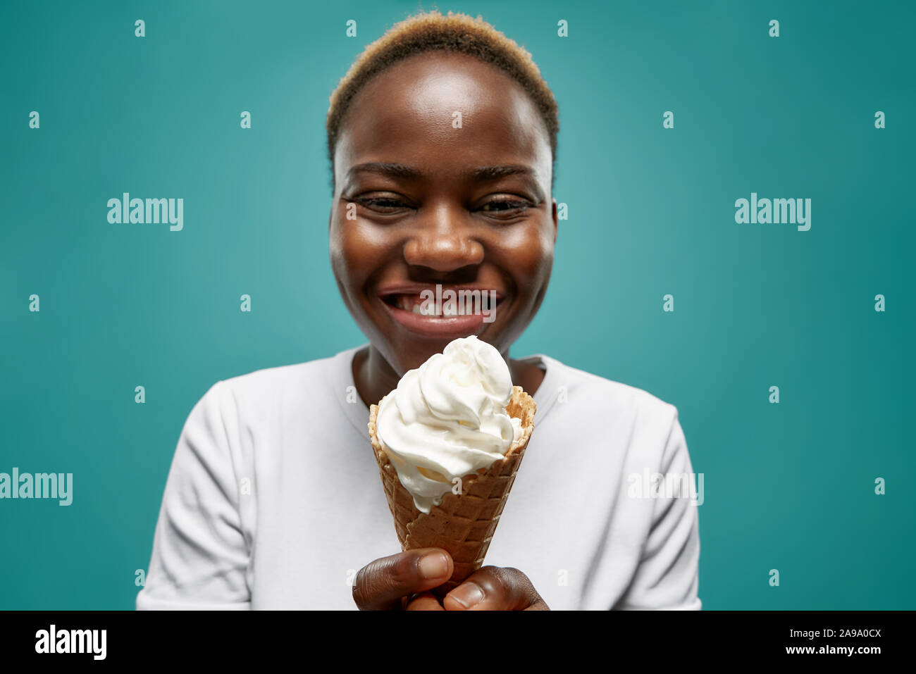 Selektiver Fokus der fröhlichen afrikanische Frau essen leckeres Eis im Sommer. Junge weibliche Waffel, an der Kamera schauen und Lachen auf blauem Hintergrund isoliert. Konzept des Genusses. Stockfoto